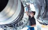 Female apprentice aircraft maintenance engineer work underneath jet engine